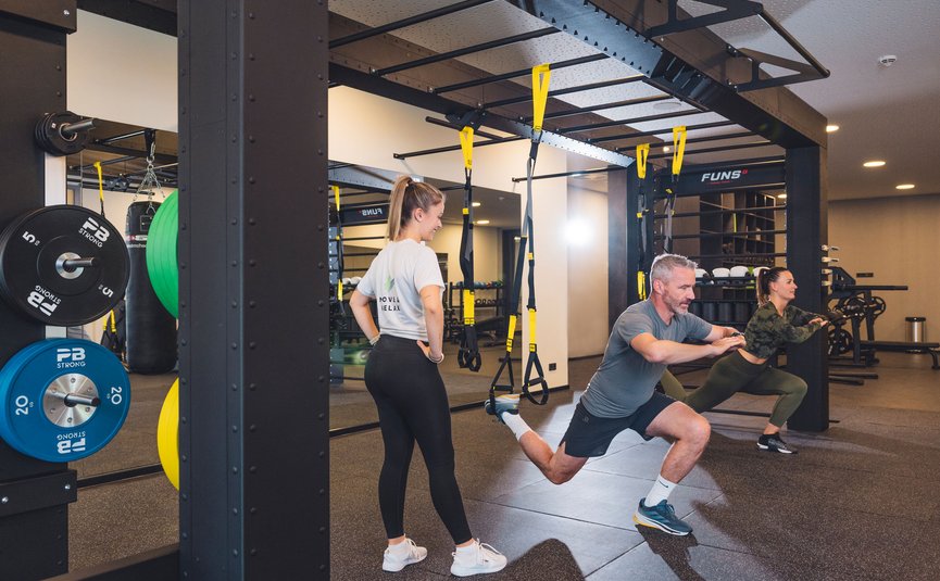 Trainer supervising man and woman doing TRX exercises in gym