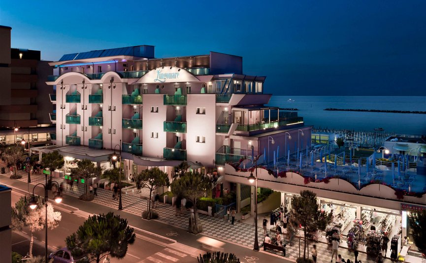 Lit-up hotel by the sea with shops and promenade at night
