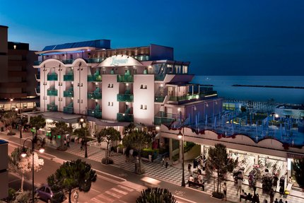 Lit-up hotel by the sea with shops and promenade at night