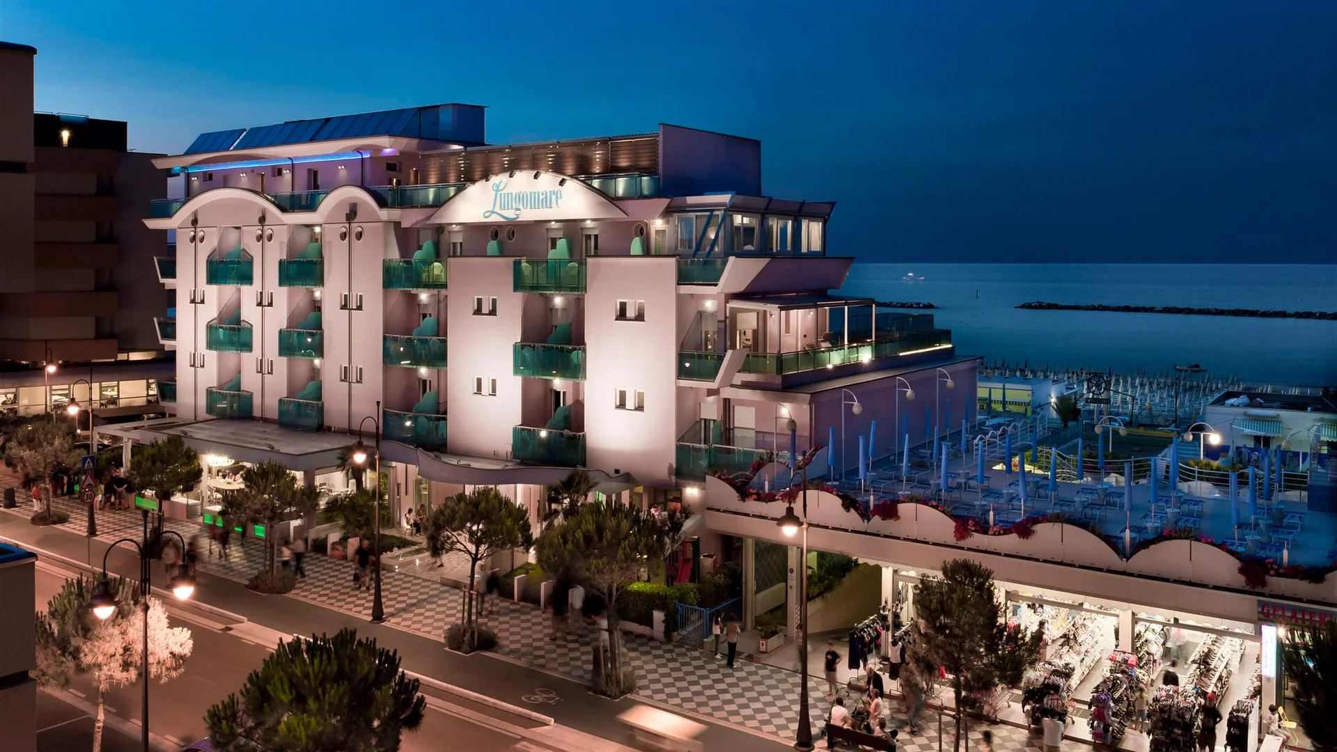 Lit-up hotel by the sea with shops and promenade at night