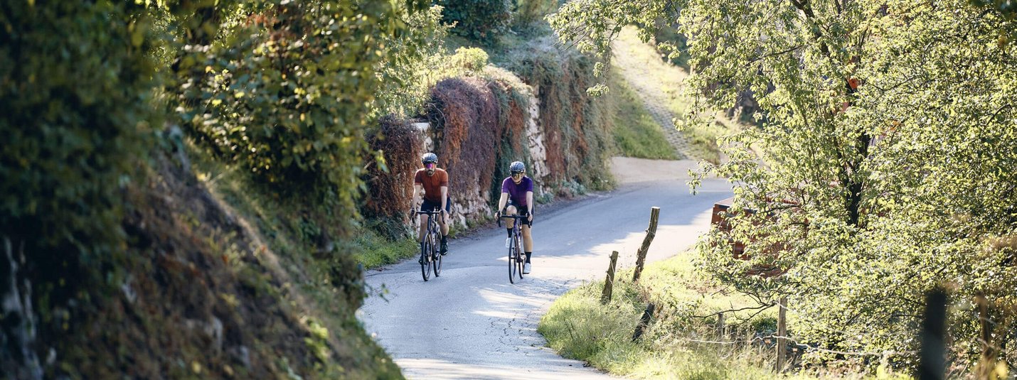 Two cyclists on a sunny country road surrounded by green trees