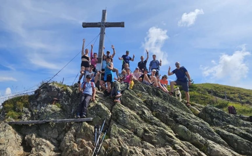 Wellness & hiking days - 3 days of nature enjoyment Group of hikers on rocky summit with large wooden cross on a sunny day