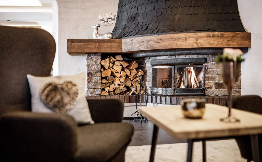 Gemütlicher Wohnraum mit Kamin, Holzstapel und Sessel mit Herz-Kissen