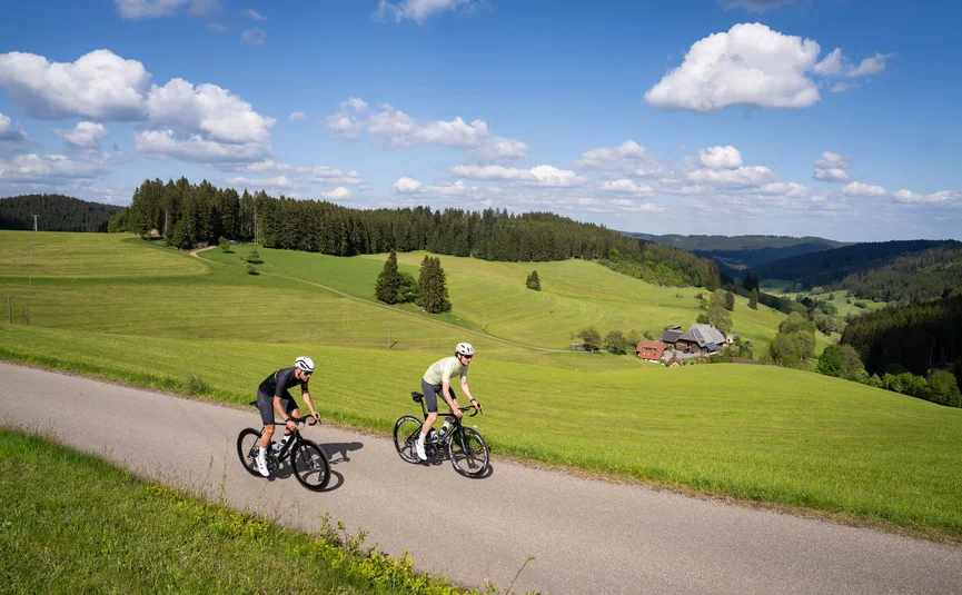 Rennrad Urlaub im Schwarzwald © Baschi Bender Zwei Radfahrer fahren auf Landstraße durch grüne Hügel und Wälder
