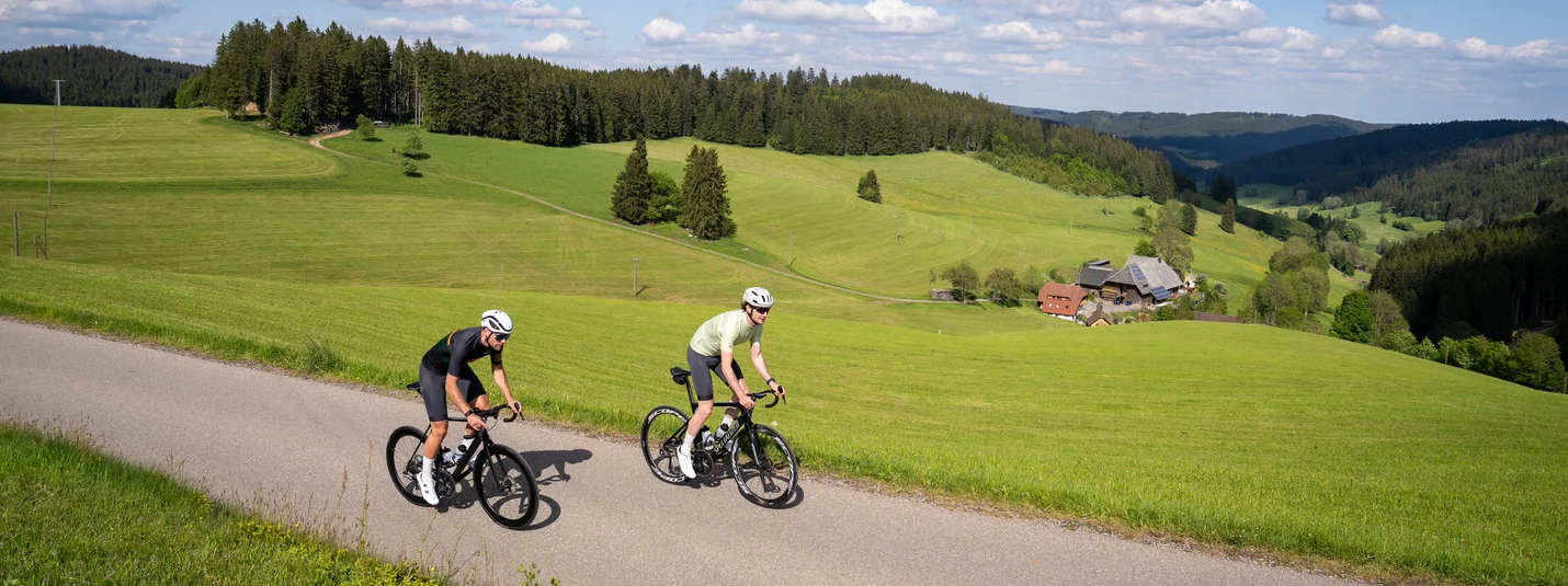 Rennrad Urlaub in Baden-Württemberg © Baschi Bender Zwei Radfahrer fahren auf Landstraße durch grüne Hügel und Wälder