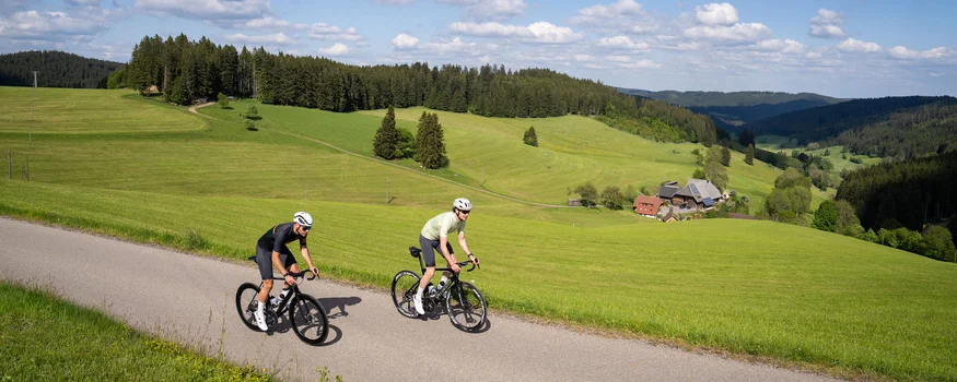 Schwarzwald © Baschi Bender Zwei Radfahrer fahren auf Landstraße durch grüne Hügel und Wälder