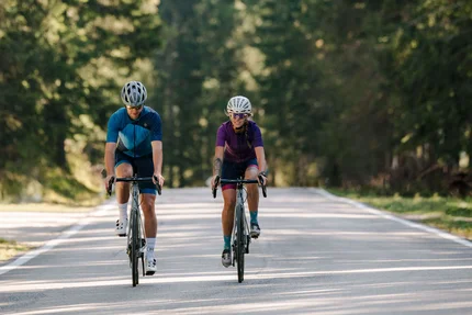 Two cyclists riding on a forest road with mountains in the background
