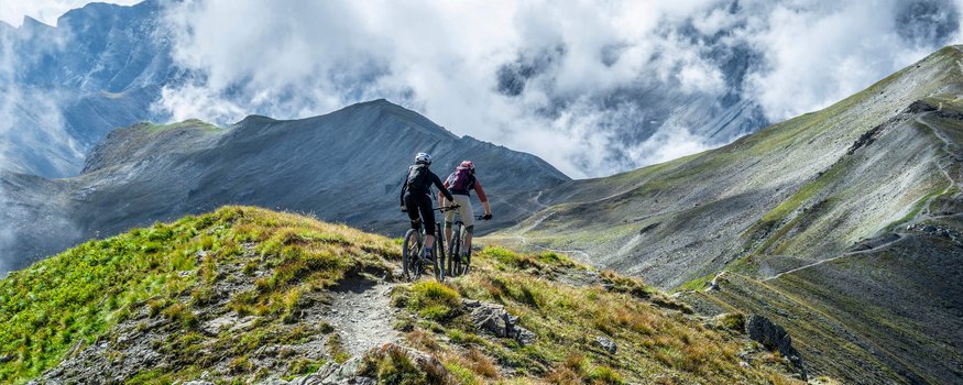 Zwei Mountainbiker fahren auf einem Bergpfad mit Nebelschwaden