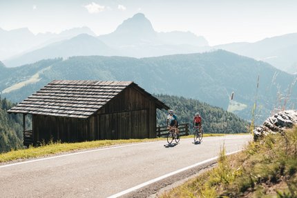 Twee wielrenners op bergweg naast houten hut in de Alpen