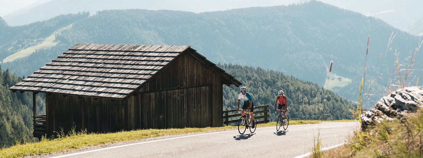 Due ciclisti su strada di montagna vicino a capanna di legno nelle Alpi