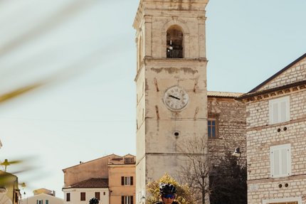 Zwei Radfahrer fahren durch eine sonnige Stadt mit einem alten Uhrturm