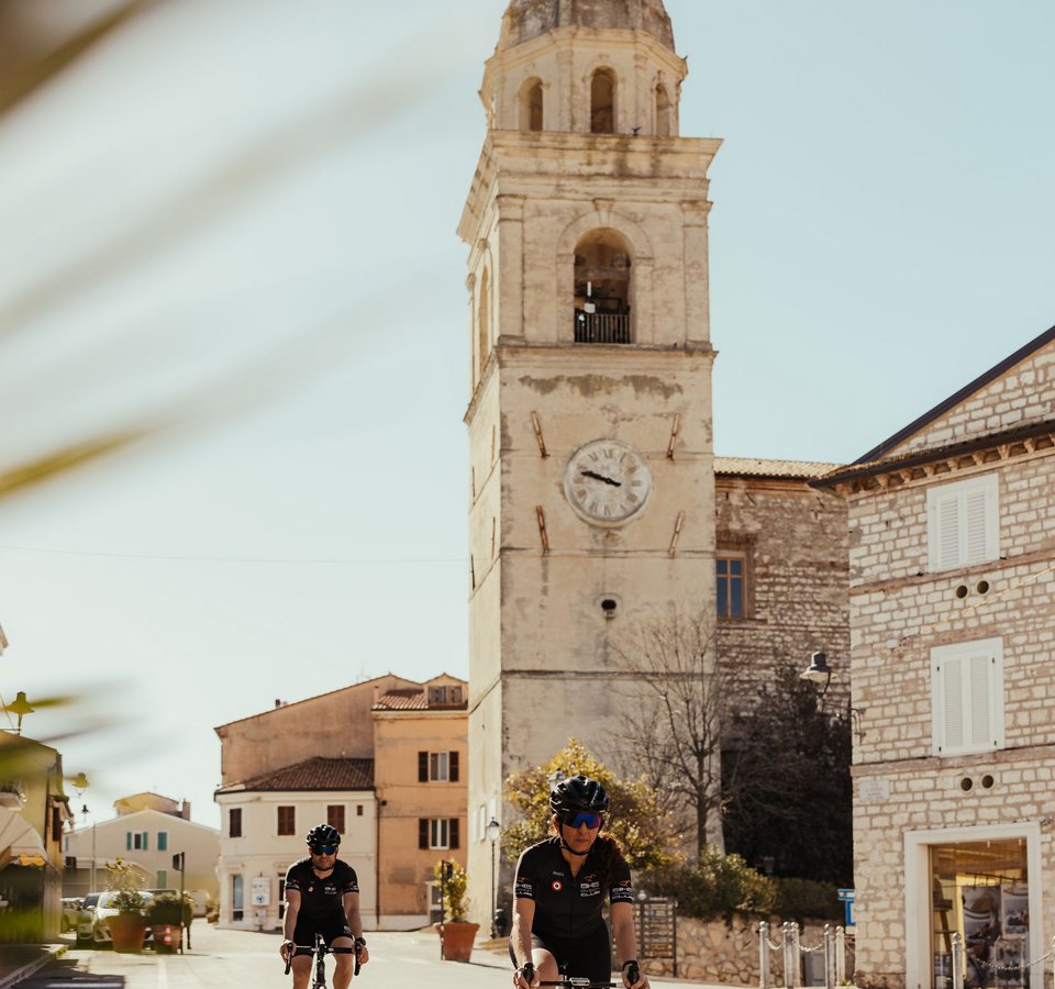 Zwei Radfahrer fahren durch eine sonnige Stadt mit einem alten Uhrturm