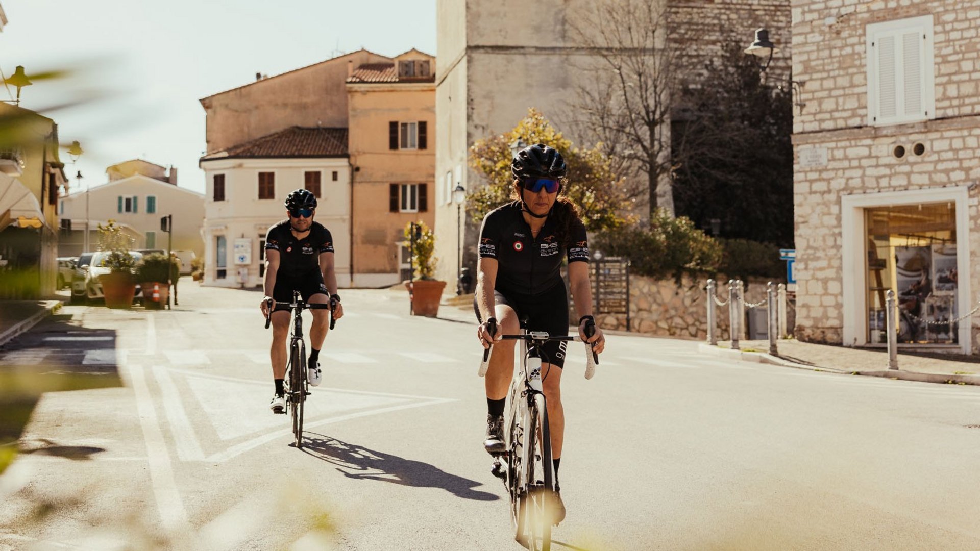 Zwei Radfahrer fahren durch eine sonnige Stadt mit einem alten Uhrturm