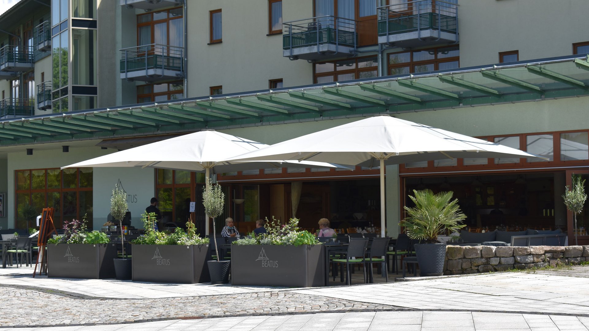 Außenterrasse eines Cafés mit weißen Sonnenschirmen und Sitzplätzen
