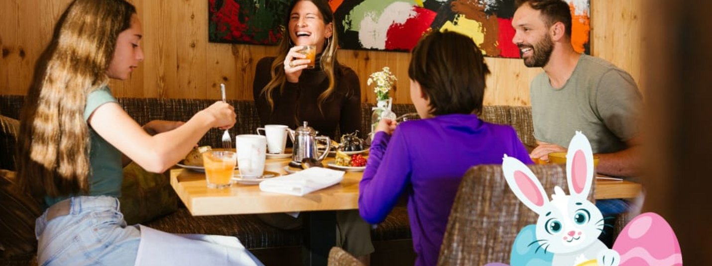 Oster-Deal für Familien: Kinder GRATIS! Familie eet en lacht in restaurant met Paashaas en geschilderde eieren