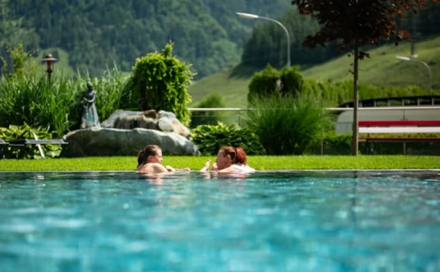 Due persone in piscina con montagne verdi e cielo nuvoloso sullo sfondo