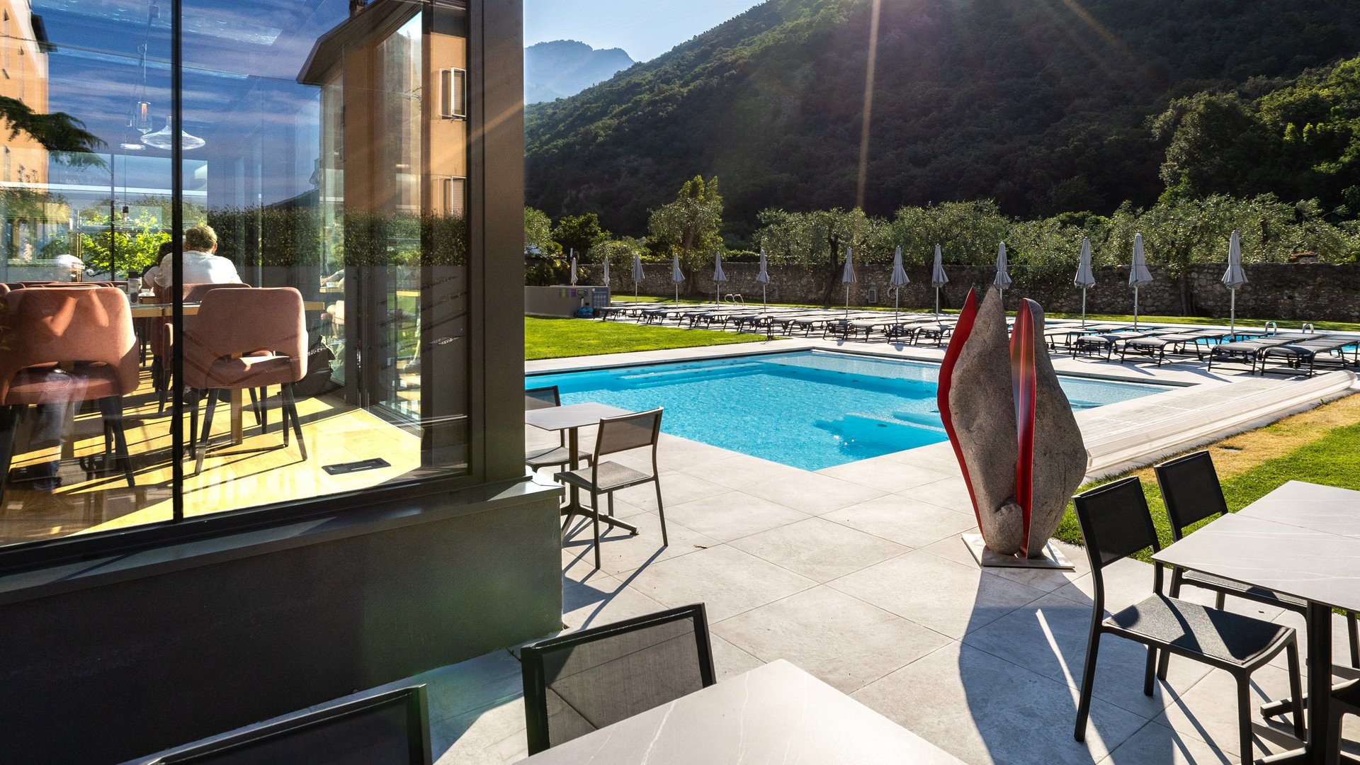 Sonniger Poolbereich mit Liegestühlen, Tischen und Bergblick