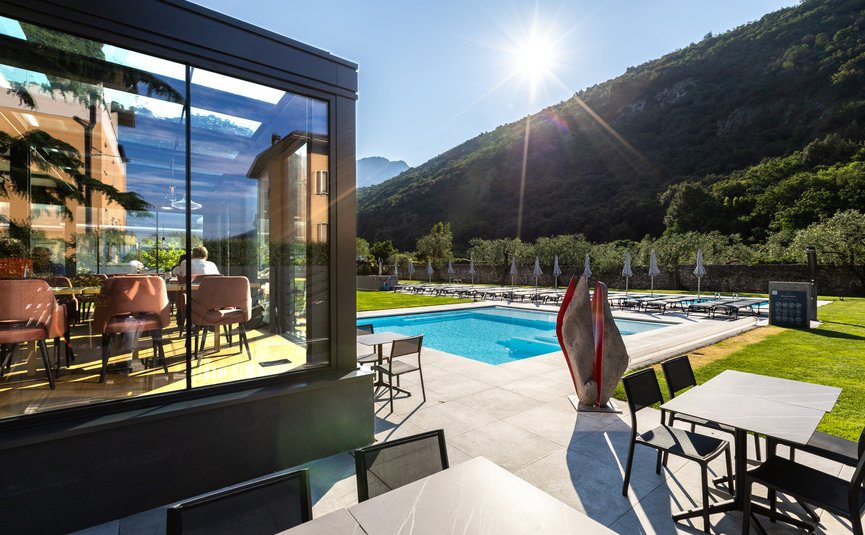 Sonniger Poolbereich mit Liegestühlen, Tischen und Bergblick