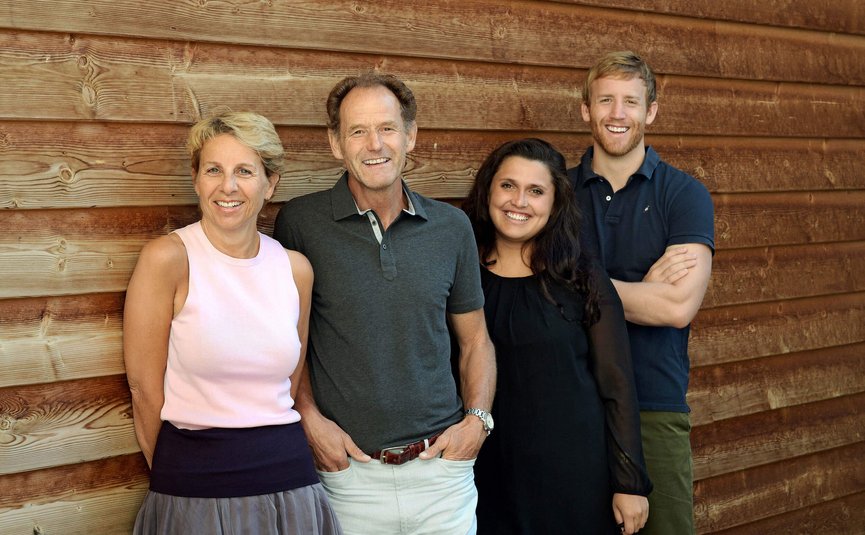 Four smiling adults standing against a wooden wall