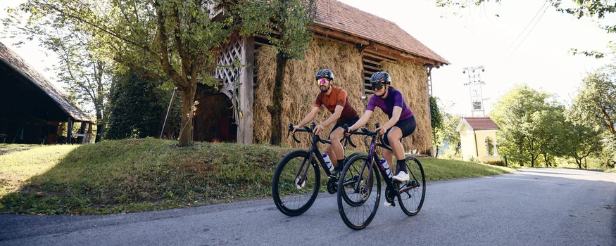 Vacanze in bici da corsa in Slovenia © Tobias Köhler Due ciclisti pedalano su strada di campagna vicino a fienile e alberi