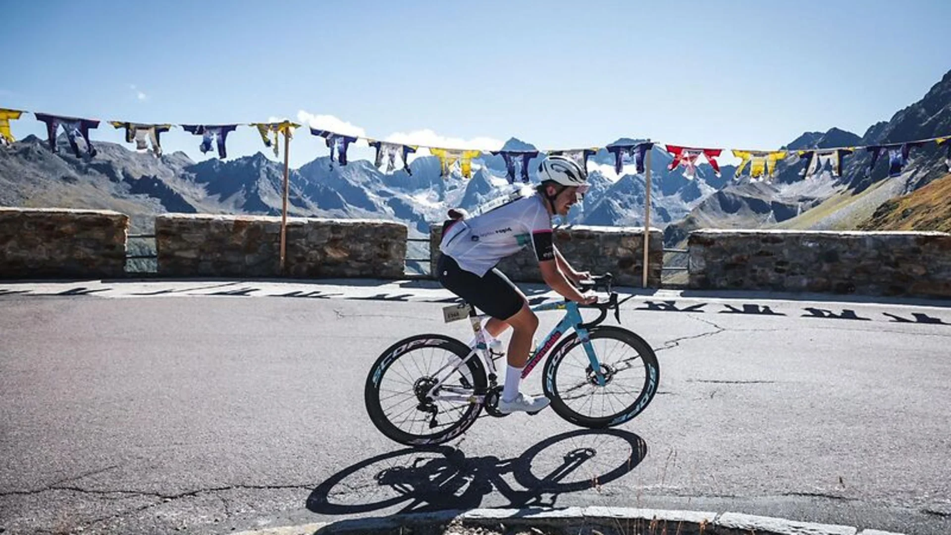 Radfahrer fährt auf Bergstraße mit Steinmauer und bunten Fahnen im Hintergrund