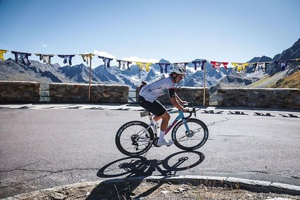 Radfahrer fährt auf Bergstraße mit Steinmauer und bunten Fahnen im Hintergrund