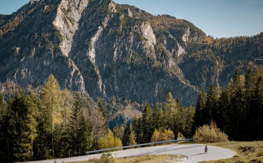 Ciclista su strada montana tortuosa con scogliere e foresta sullo sfondo