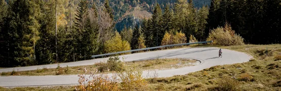 Ciclista su strada montana tortuosa con scogliere e foresta sullo sfondo