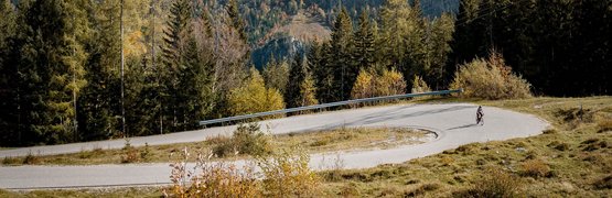 Cyclist on winding mountain road with cliffs and forest in background