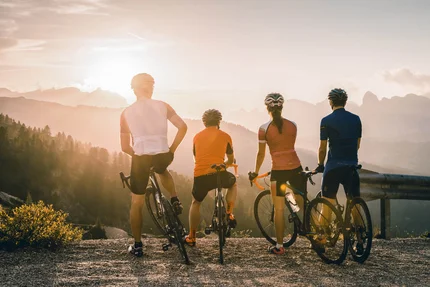 Quattro ciclisti guardano il paesaggio montano al tramonto