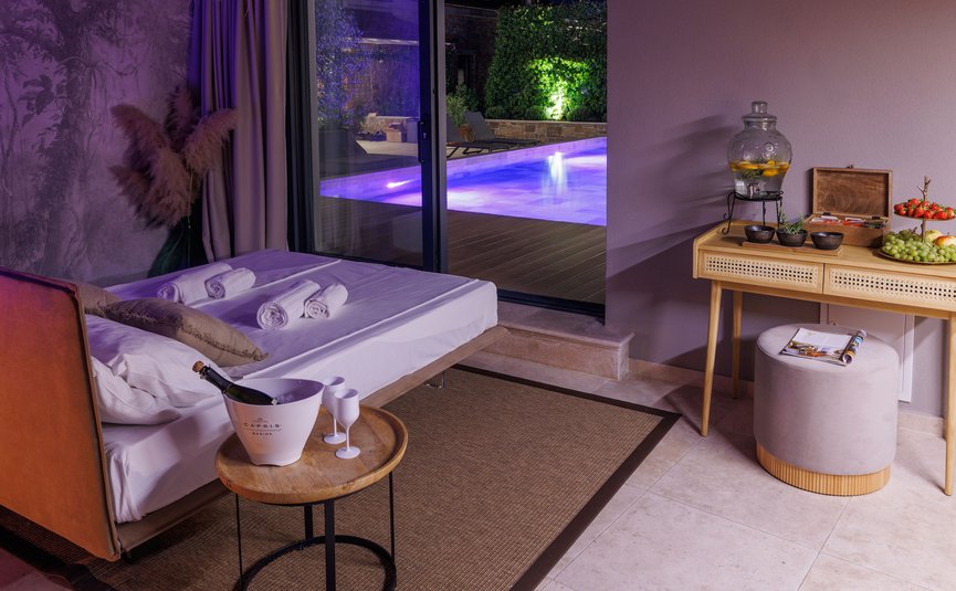 Modern room with bed, drinks table, and view of illuminated pool at night
