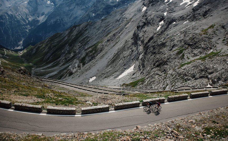 Twee fietsers op kronkelende bergweg met steile rotskliffen