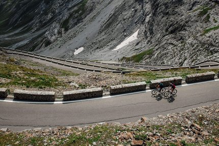 Two cyclists on winding mountain road with steep rocky cliffs