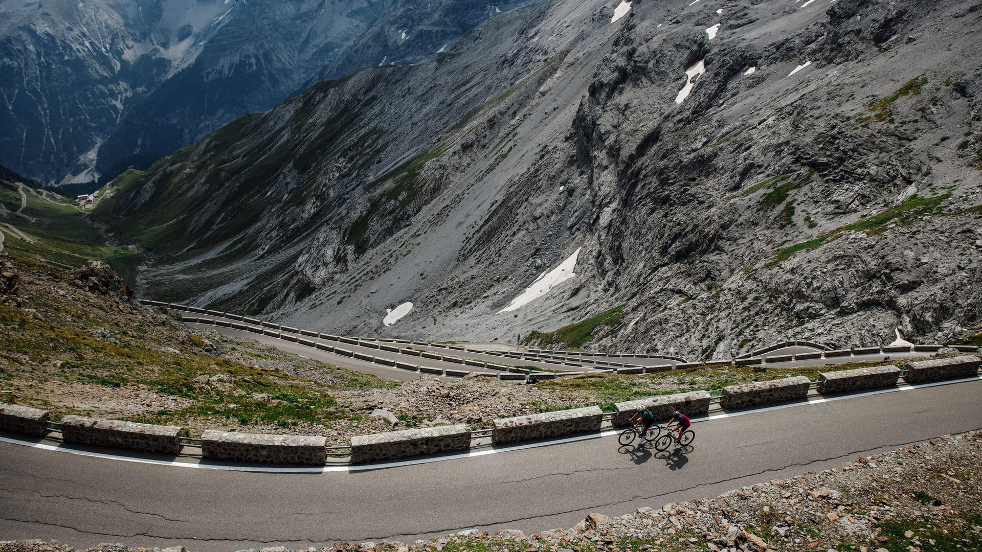 Two cyclists on winding mountain road with steep rocky cliffs