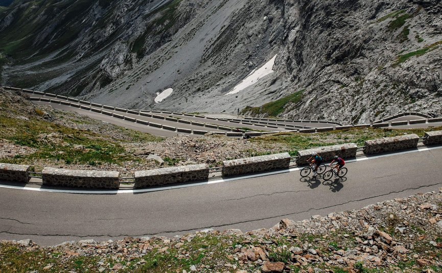 Two cyclists on winding mountain road with steep rocky cliffs