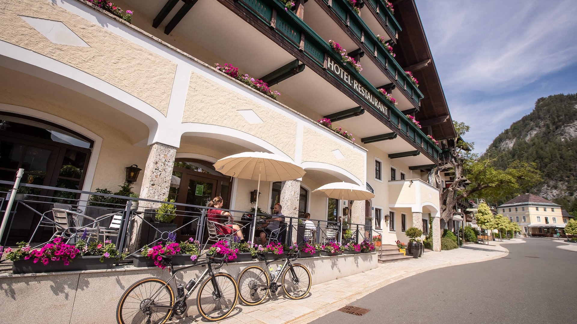 Außenbereich eines Hotels mit Terrasse, Fahrrad und Bergen im Hintergrund