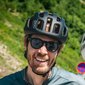 Two cyclists wearing helmets smiling and talking on a road in greenery