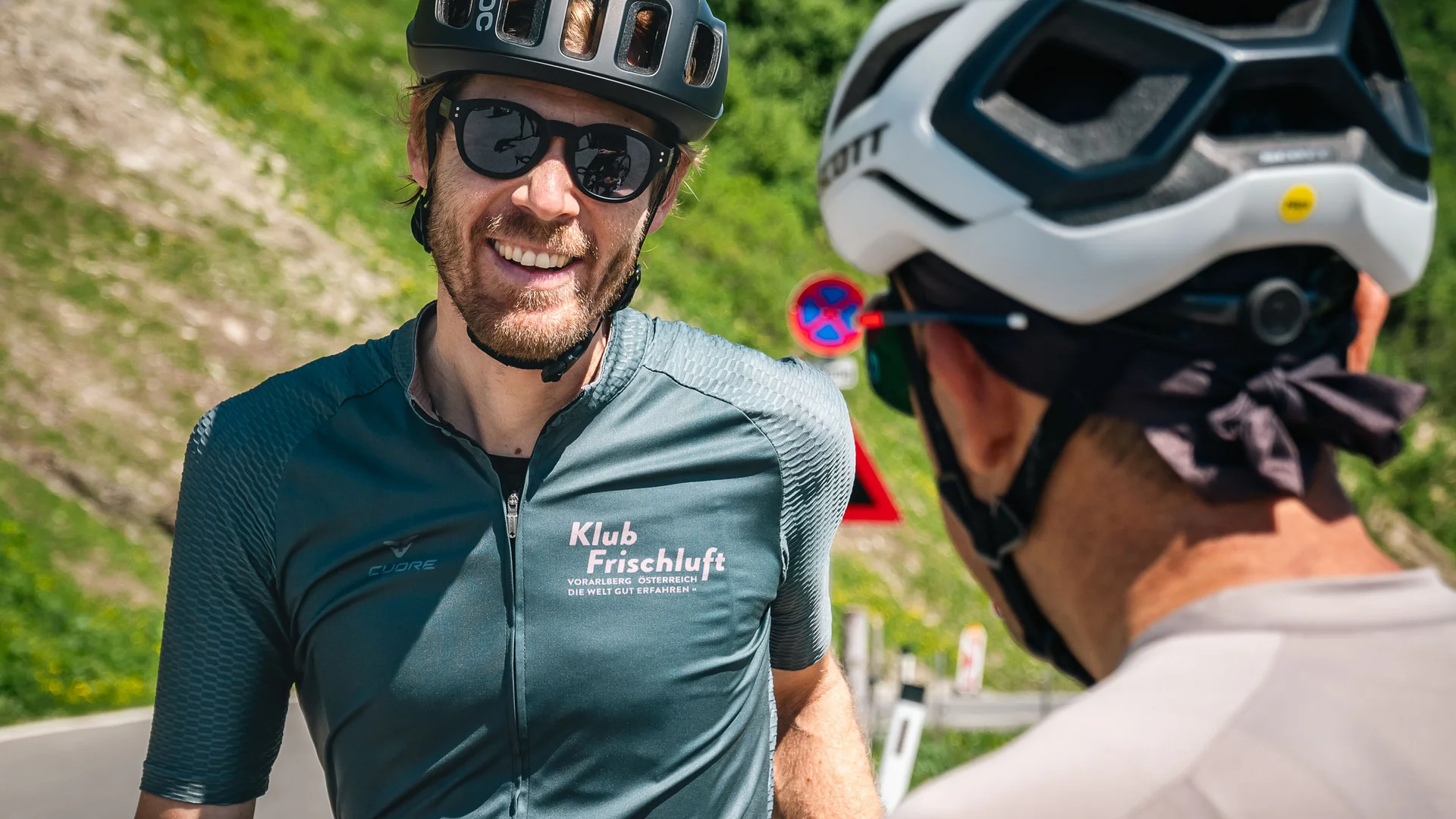 A racing bike weekend in the Bregenzerwald © Alain Rumpf - A Swiss With A Pulse Two cyclists wearing helmets smiling and talking on a road in greenery