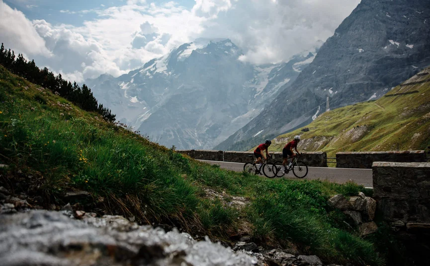 Due ciclisti su strada di montagna con montagne nuvolose sullo sfondo