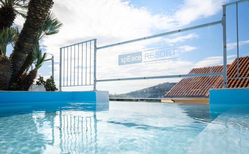 Vista di una piscina con recinzione in vetro e palme in una giornata di sole