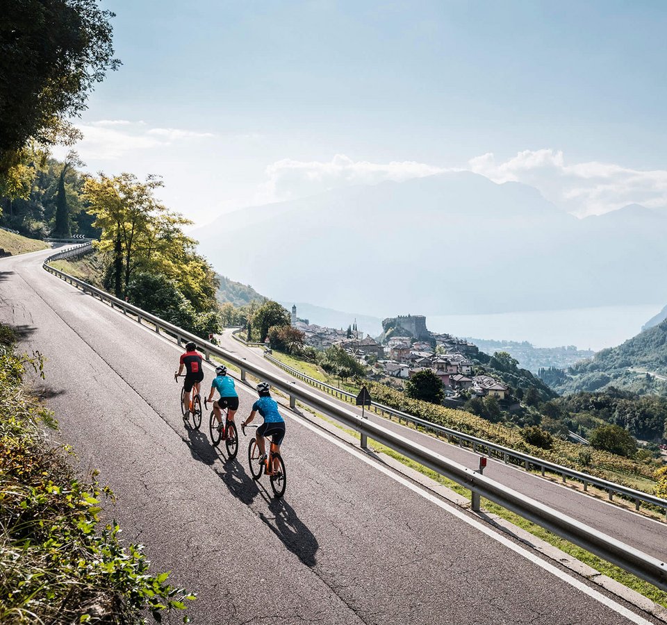 Drei Radfahrer fahren auf Bergstraße mit Blick auf Dorf und See