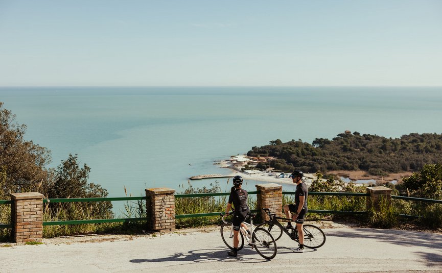 Due ciclisti su strada di montagna con vista sul mare in una giornata soleggiata