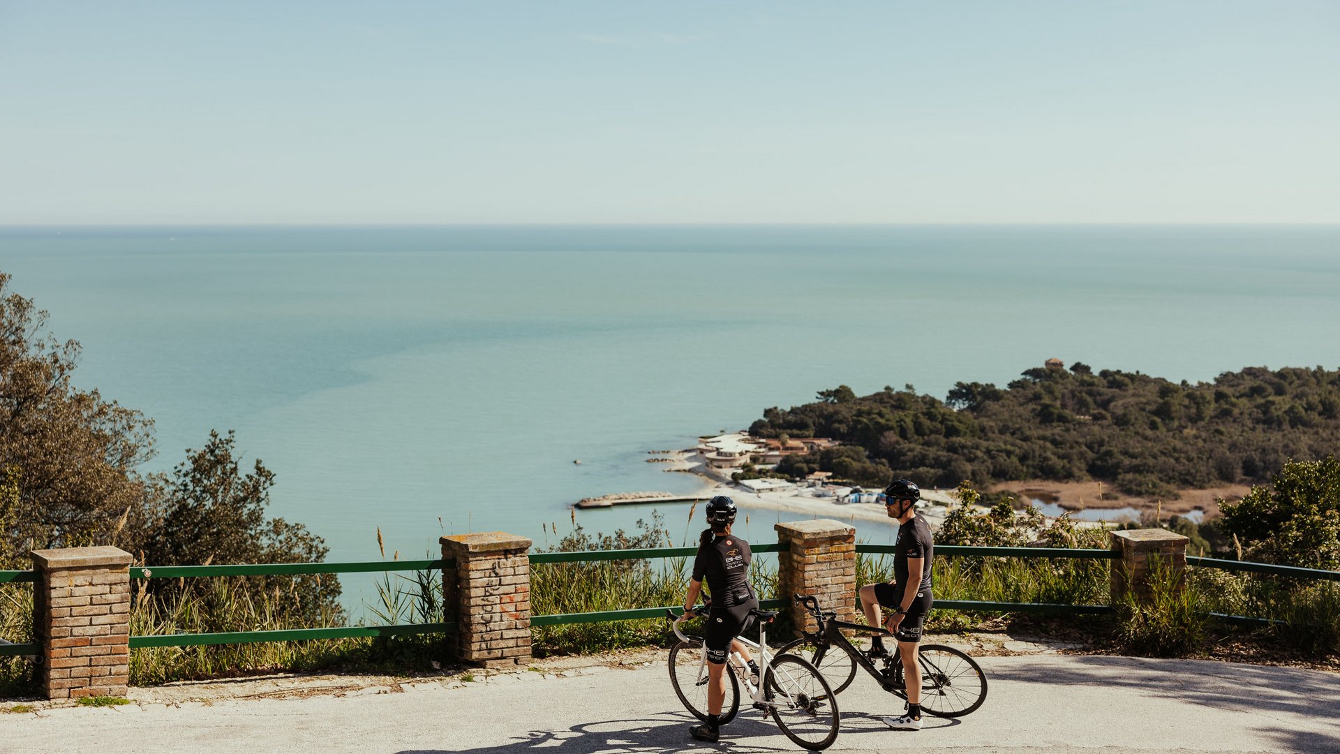 Zwei Radfahrer auf Bergstraße mit Meerblick bei sonnigem Wetter