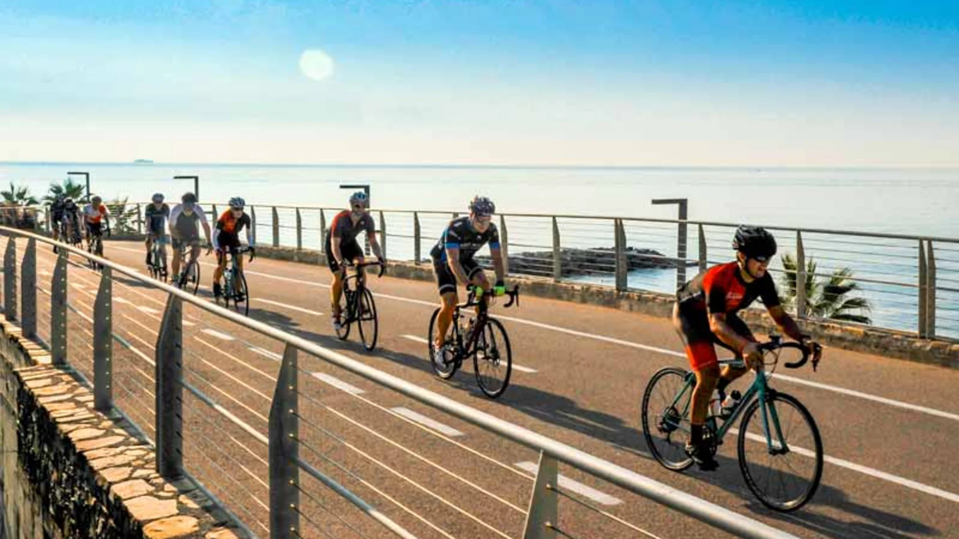 Group of cyclists riding along the seaside promenade on a sunny day