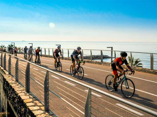 Villa Giada SpEace Resort: Mit deinem Rennrad aufs Zimmer © Villa Giada spEace & Bike Resort Gruppe von Radfahrern fährt an der Meerespromenade bei sonnigem Wetter