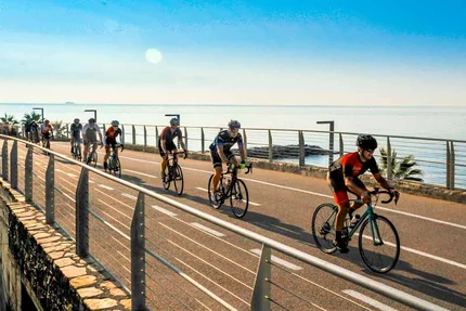 Group of cyclists riding along the seaside promenade on a sunny day