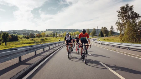 Vier fietsers rijden op een landweg door een groen landschap.