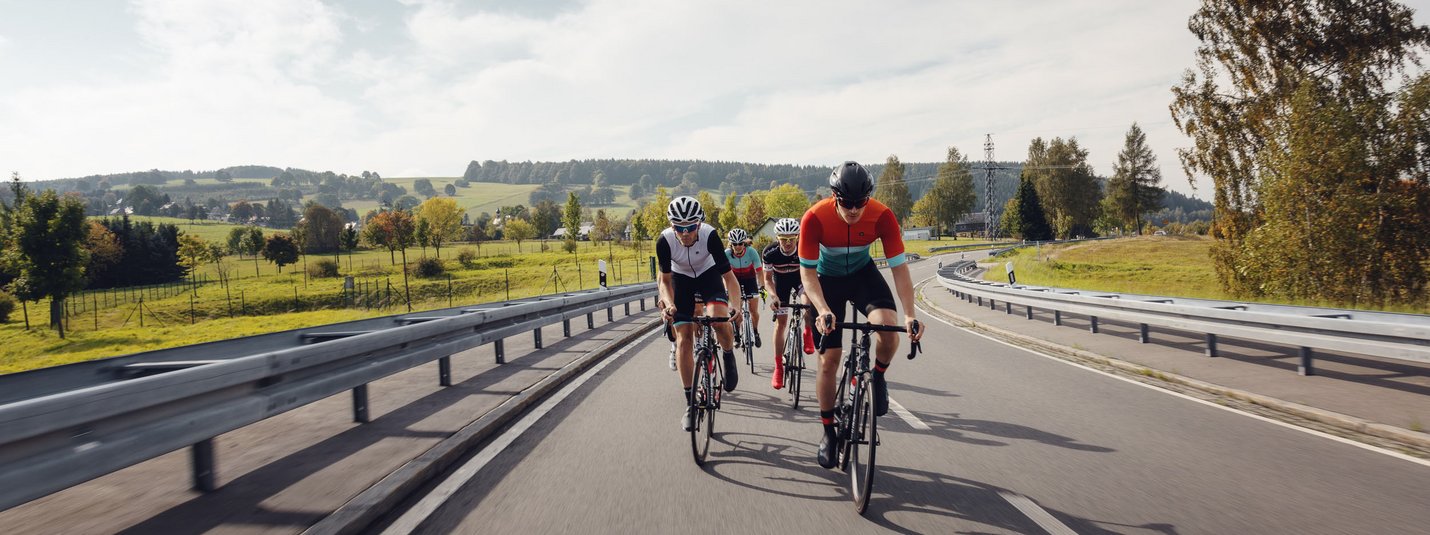 Vier Radfahrer fahren auf einer Landstraße durch eine grüne Landschaft.