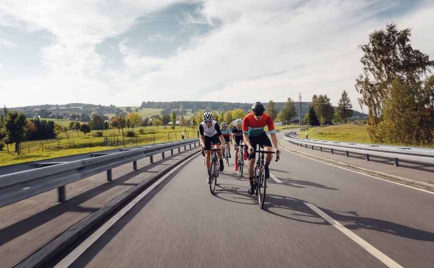 Quattro ciclisti pedalano su una strada di campagna in un paesaggio verde.