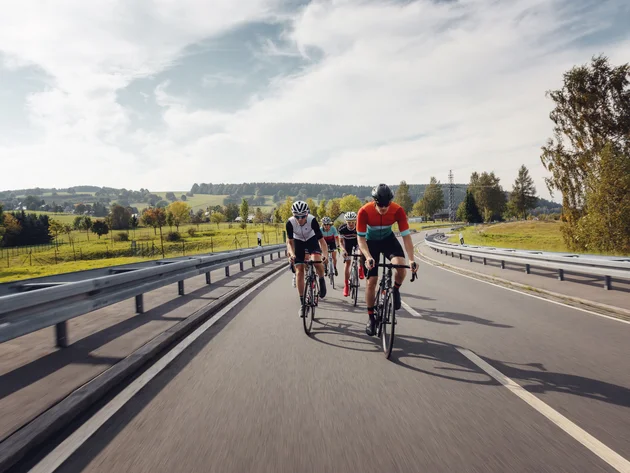 Vier fietsers rijden op een landweg door een groen landschap.
